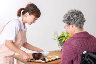 高齢女性に食事を出す医療従事者の女性の画像