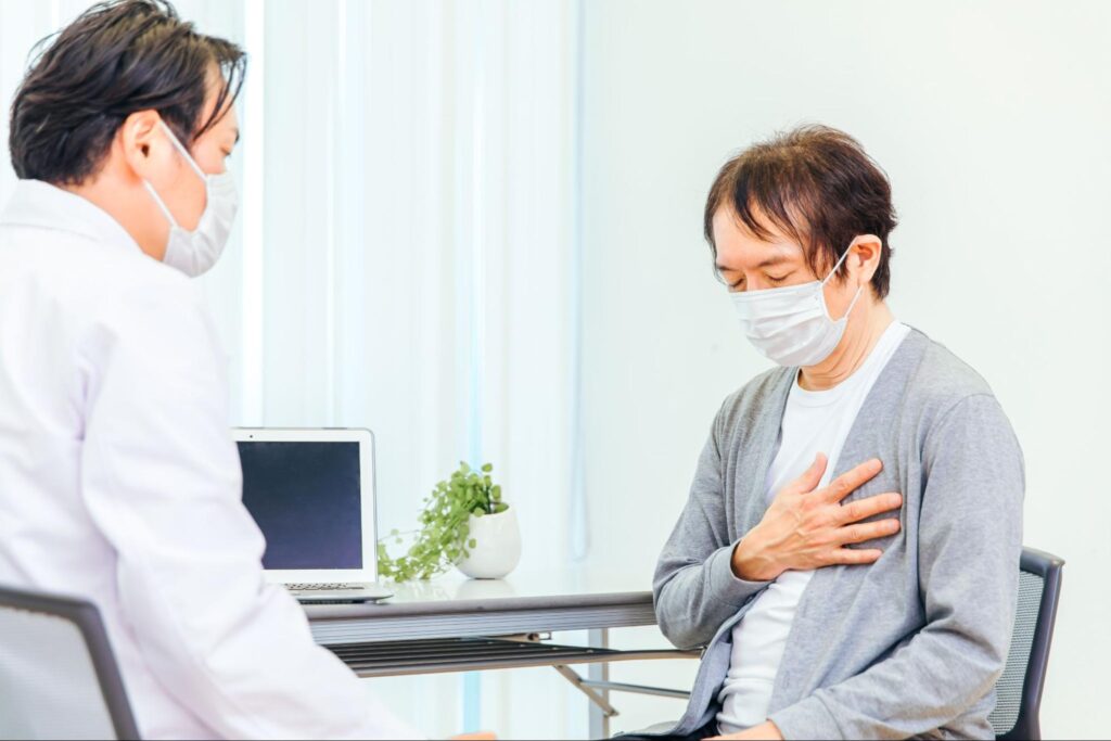 胸元を押さえる高齢男性と男性医師