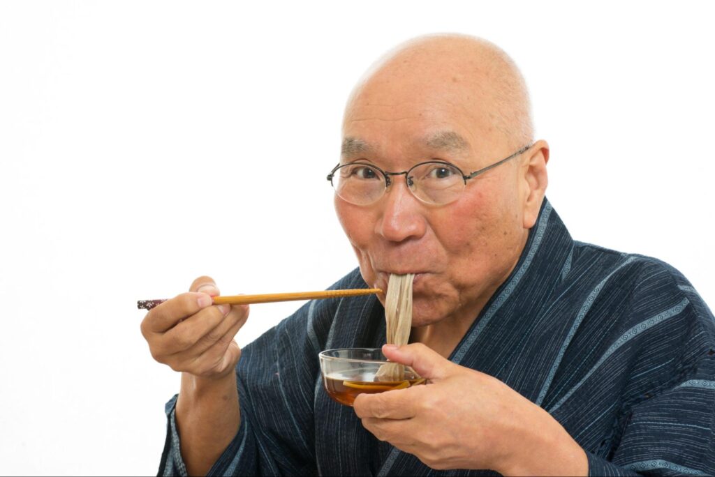そばをすする高齢男性の画像