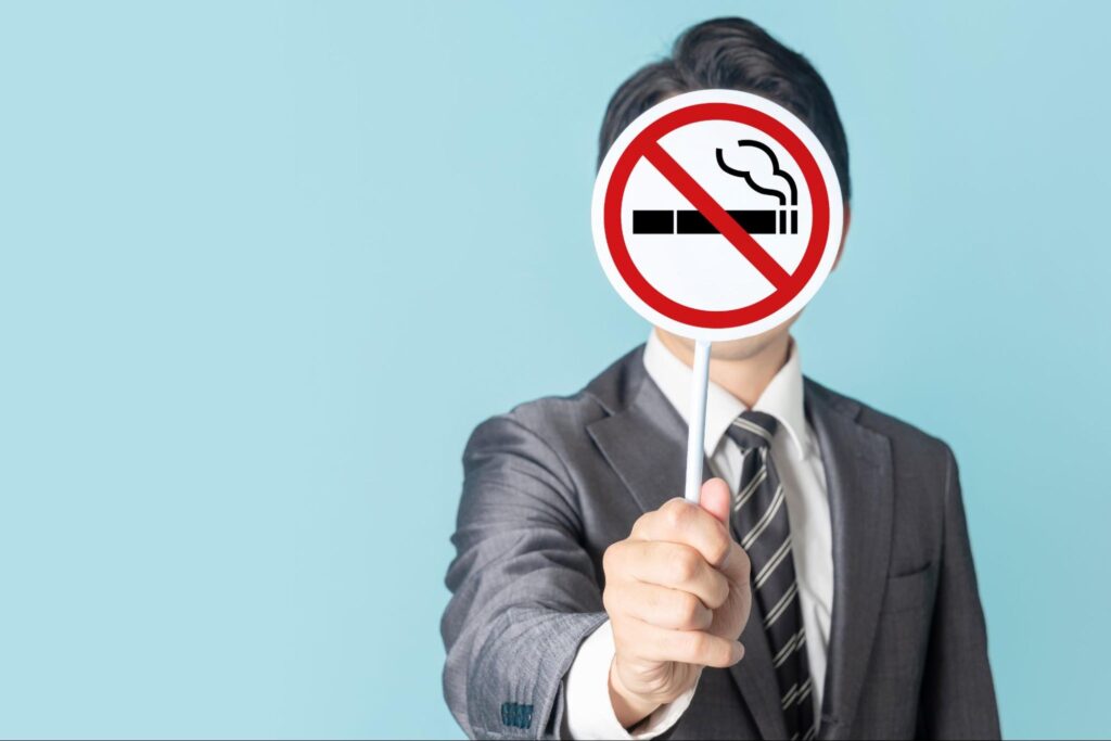 禁煙マークをかざすスーツ姿の男性