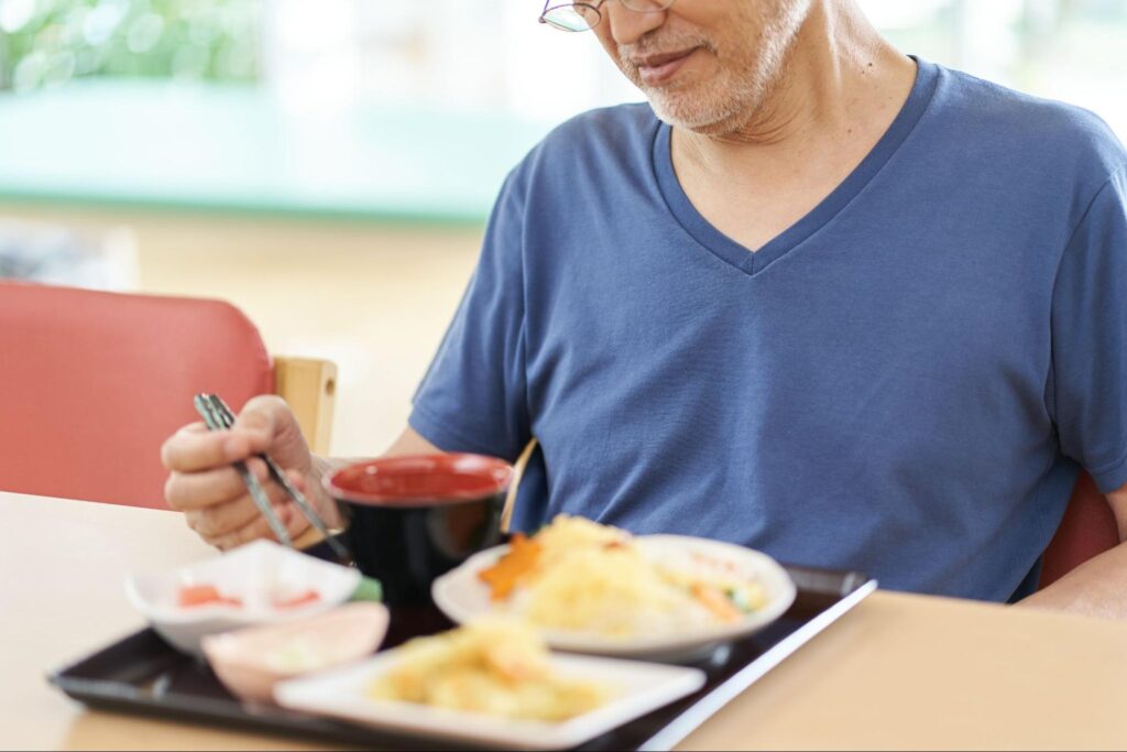 浮かない顔で食事をする高齢男性
