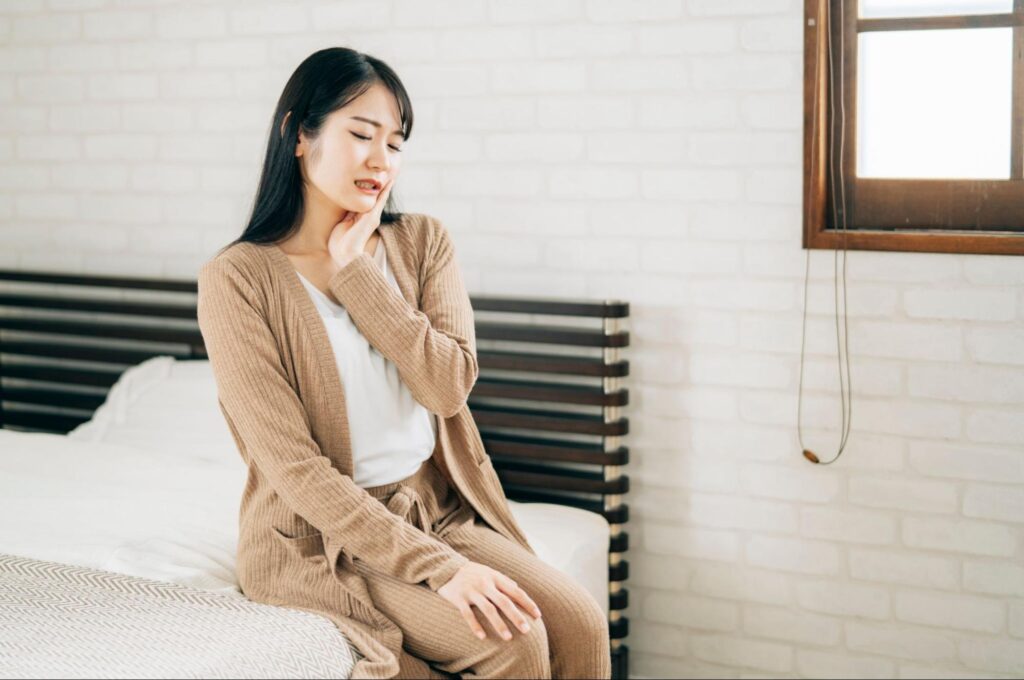 抜歯後に腫れ痛みが出て、頬を押さえている女性